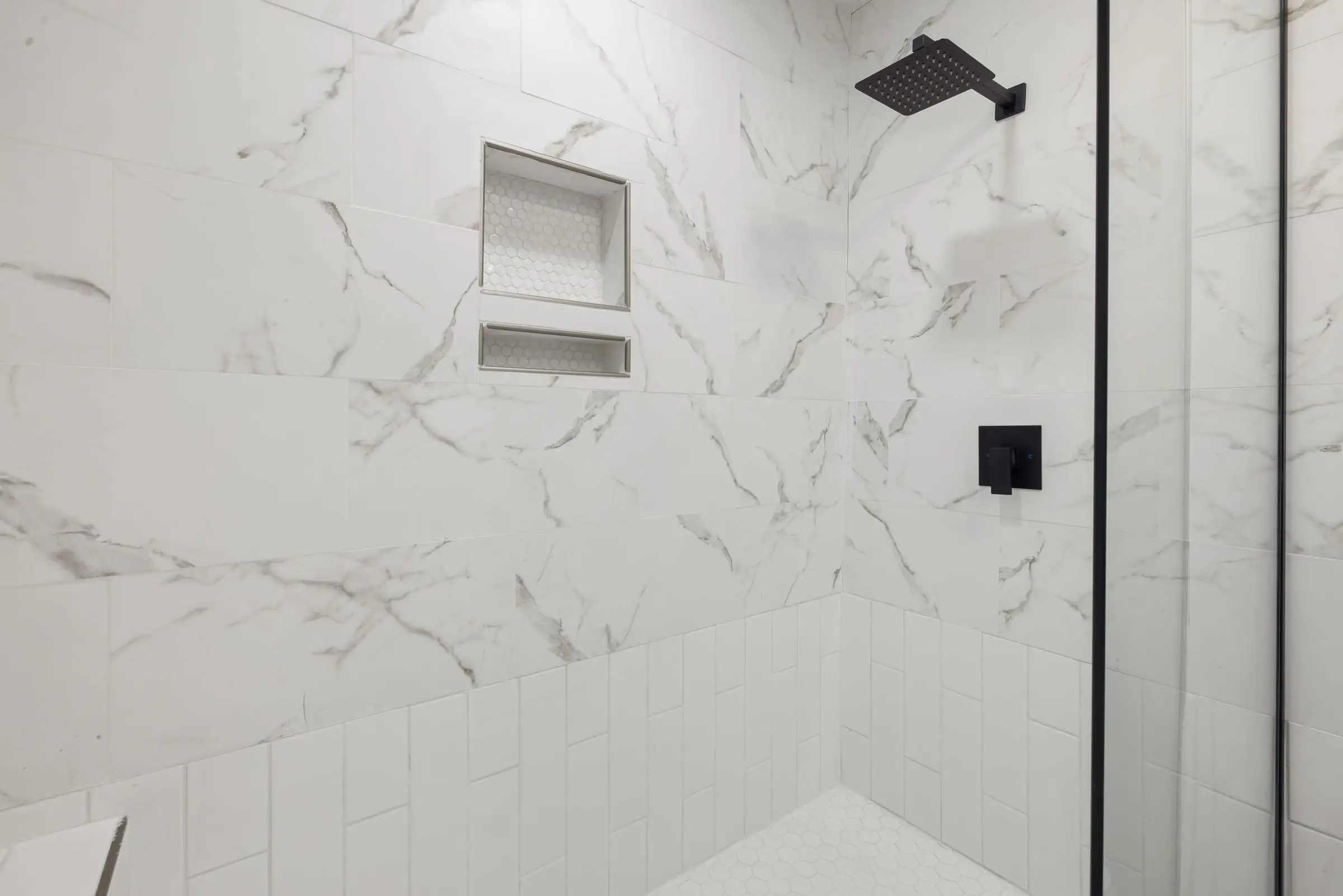 Douche à l’italienne en marbre blanc veiné de gris, niche encastrée dans le mur, pommeau noir, paroi de verre fixe