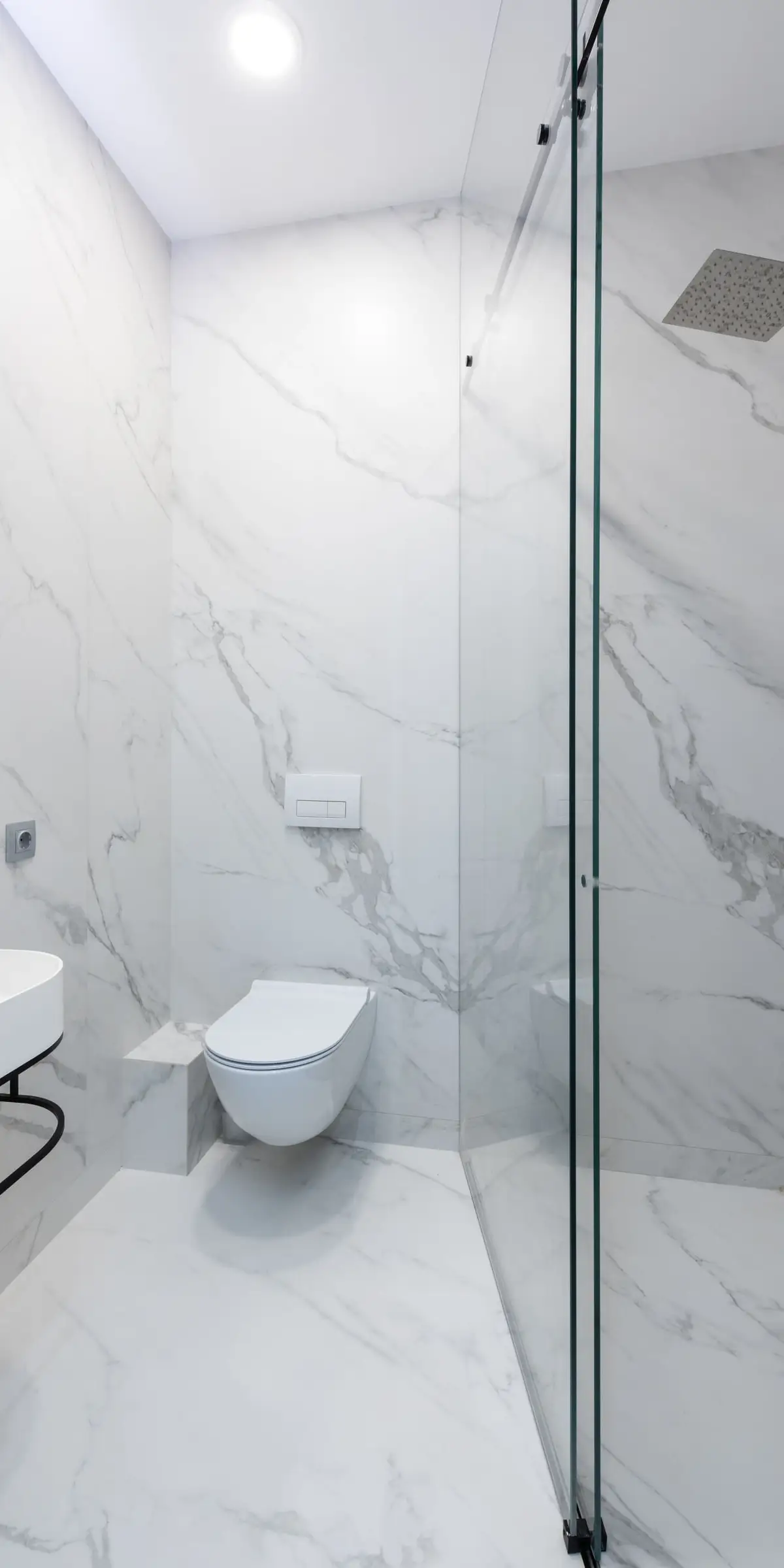 Douche de plain-pied en pierre blanche veinée de gris, paroi de verre sans cadre, sol continu jusqu’au lavabo