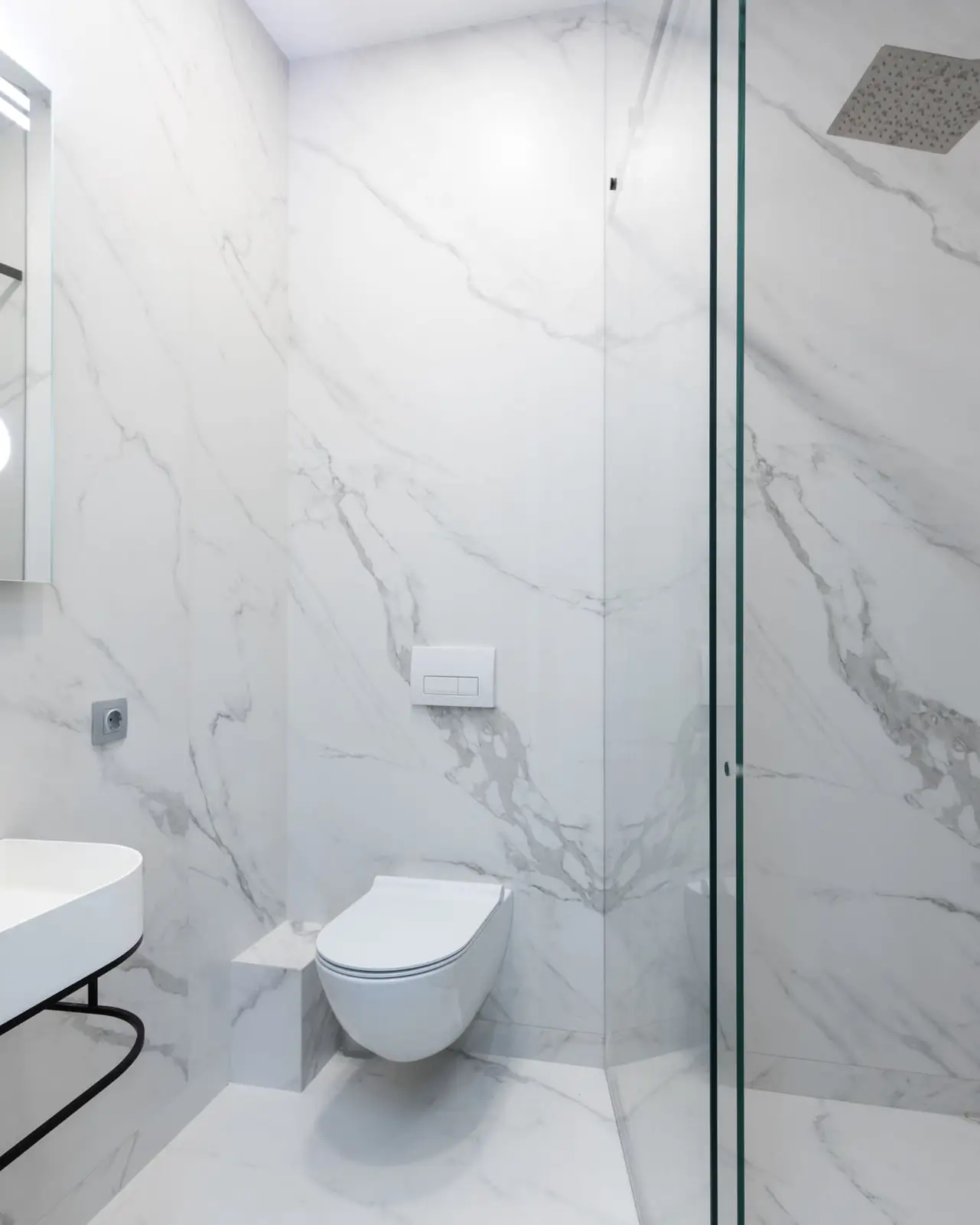 La même salle de bain vue plus large, lavabo blanc sur console noire, miroir rétroéclairé, murs en grandes dalles veinées