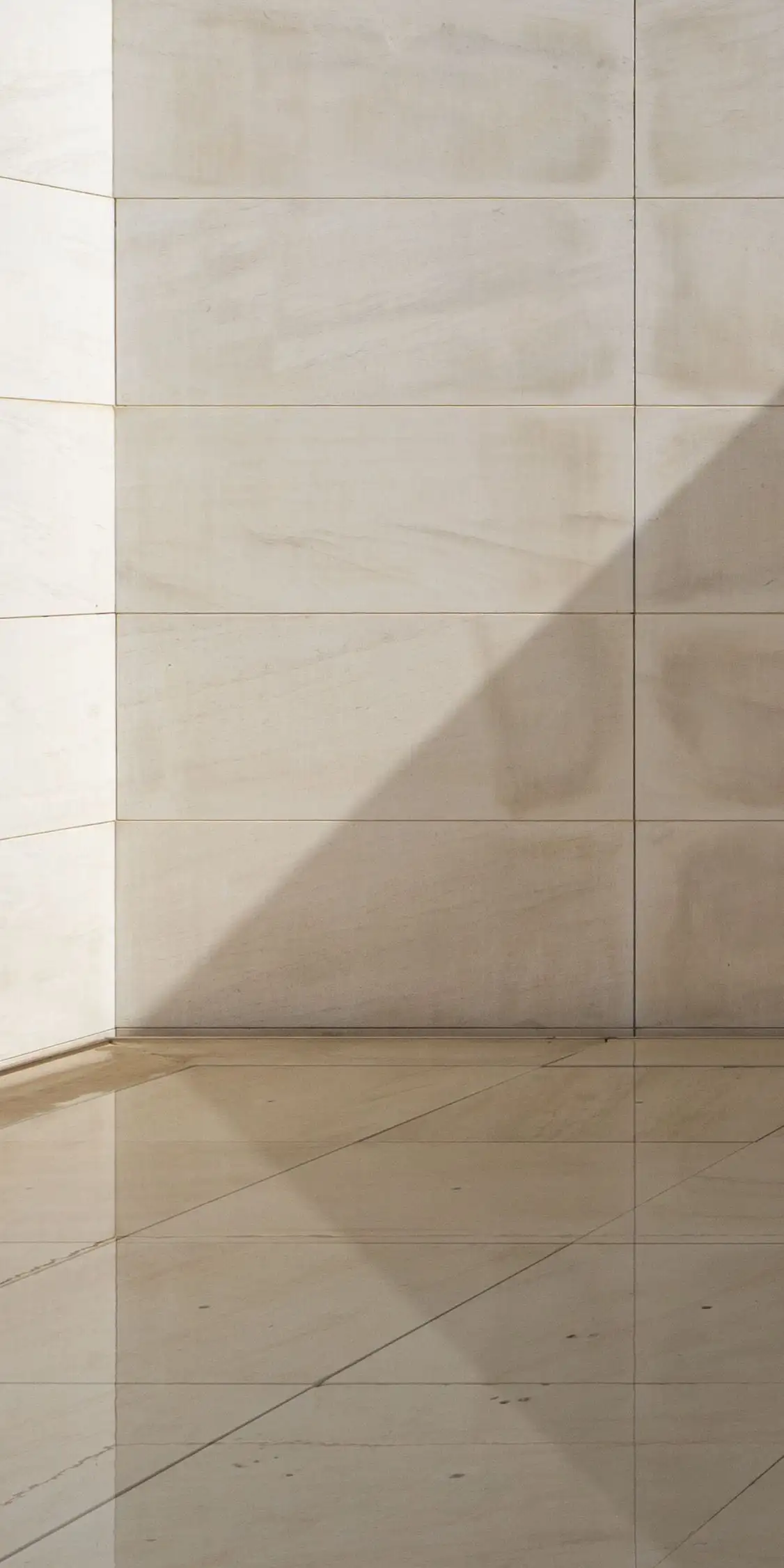 Angle d’une entrée en pierre calcaire blanche, mur et sol de la même pierre en grandes dalles, ombre portée d’une fenêtre