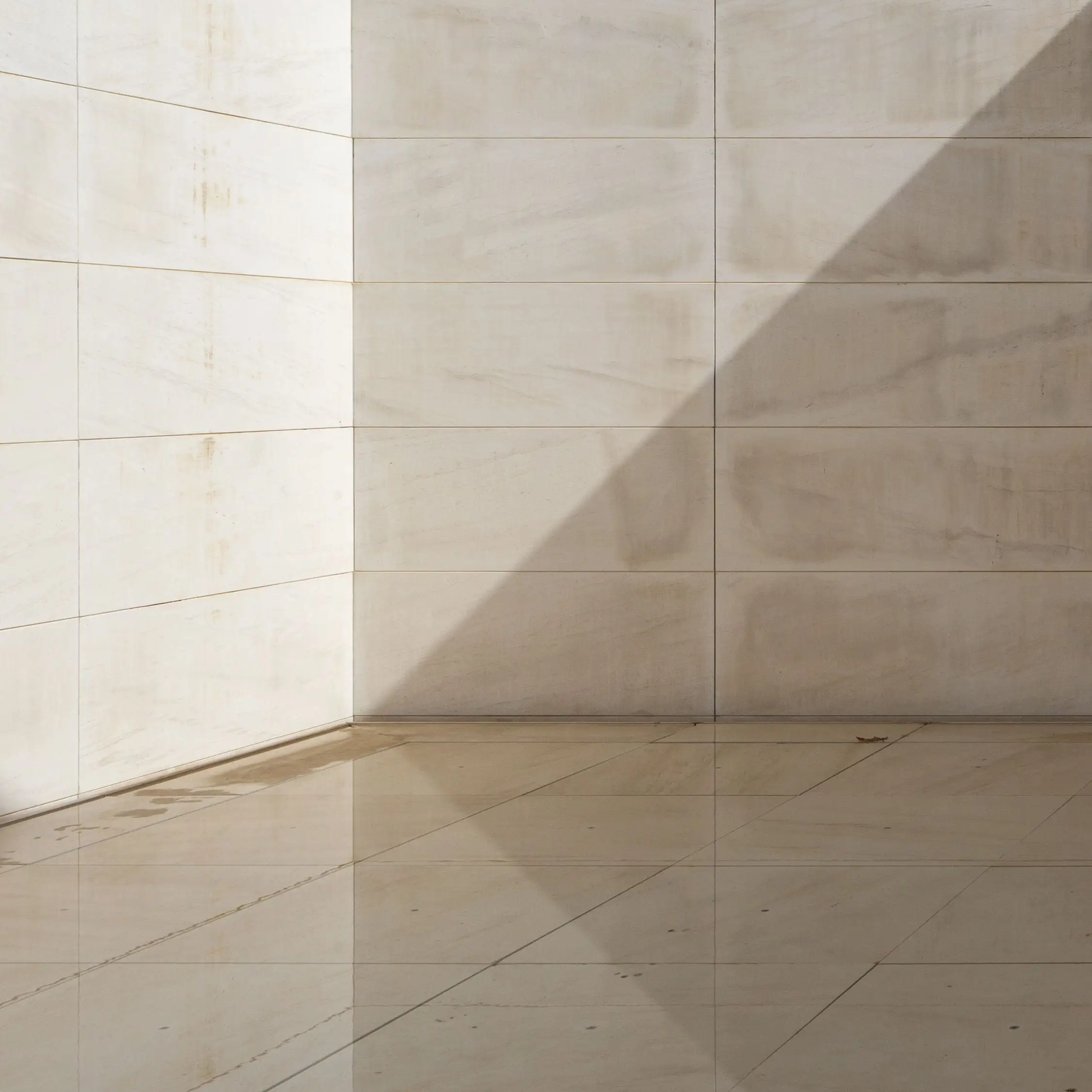 Angle d’une entrée en pierre calcaire blanche, mur et sol de la même pierre en grandes dalles, ombre portée d’une fenêtre