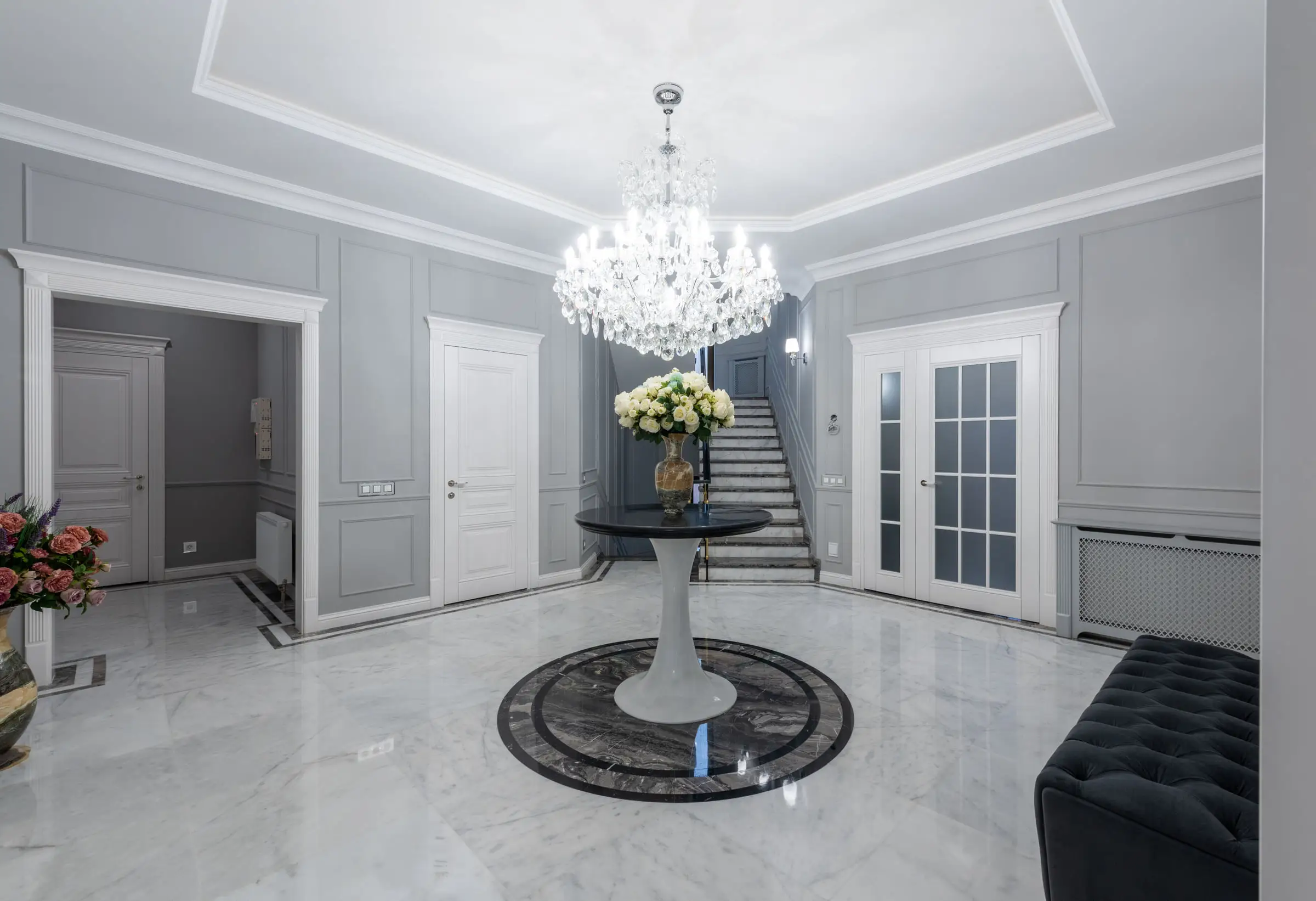Hall d’entrée au sol de marbre clair poli avec médaillon circulaire sombre, escalier au fond, portes blanches