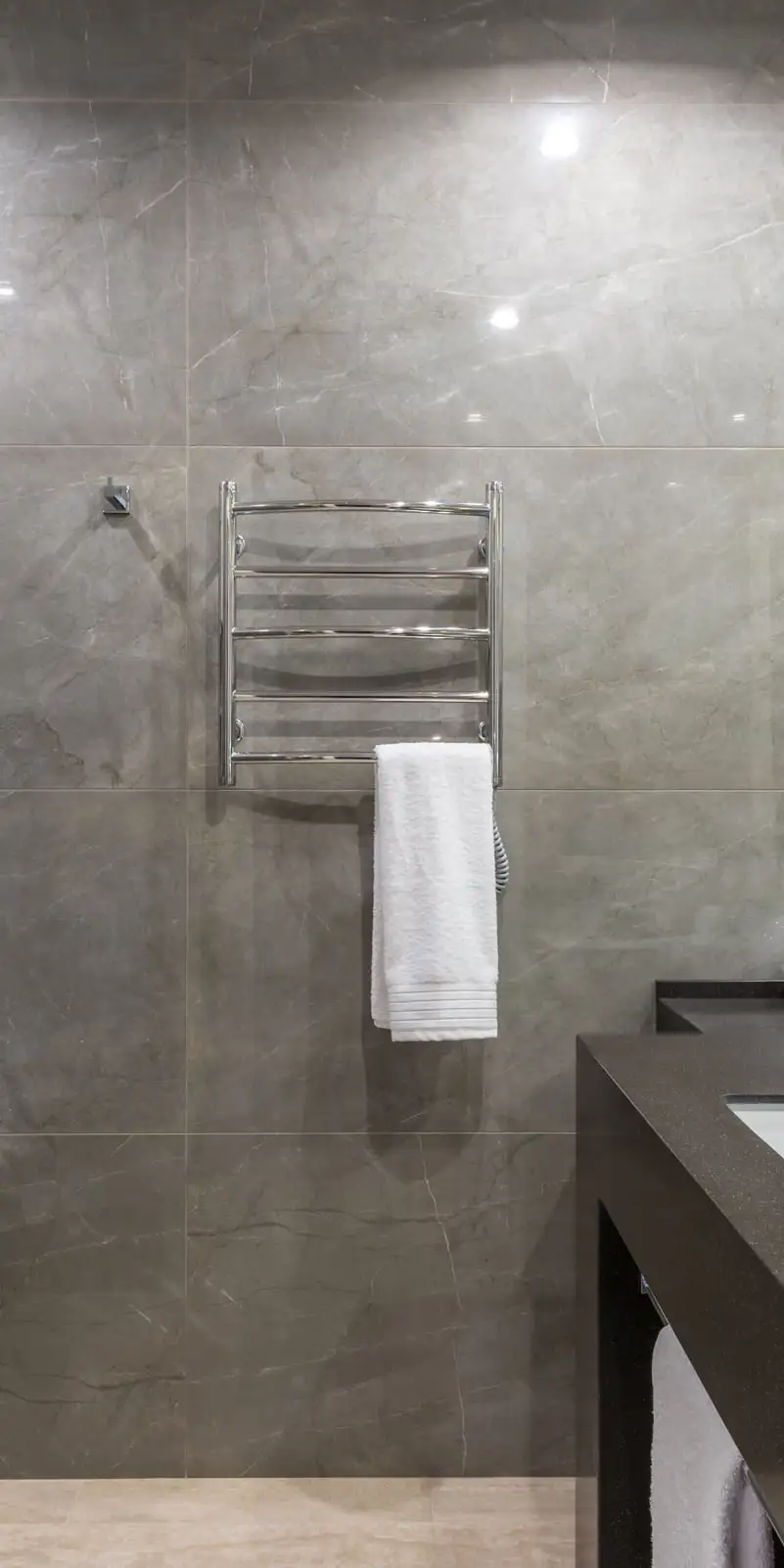 Salle de bain en pierre grise sombre, plan de toilette noir, paroi de douche en verre, sèche-serviettes chromé