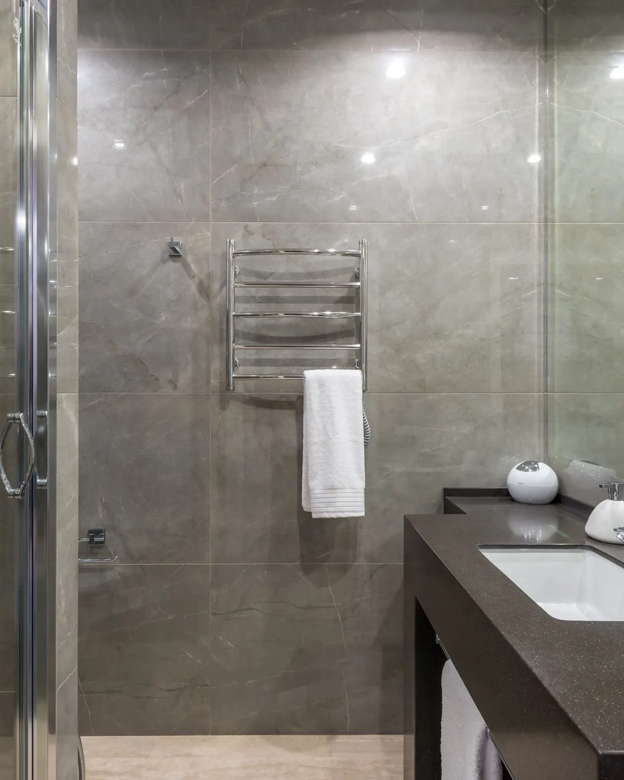 Salle de bain en pierre grise sombre, plan de toilette noir, paroi de douche en verre, sèche-serviettes chromé