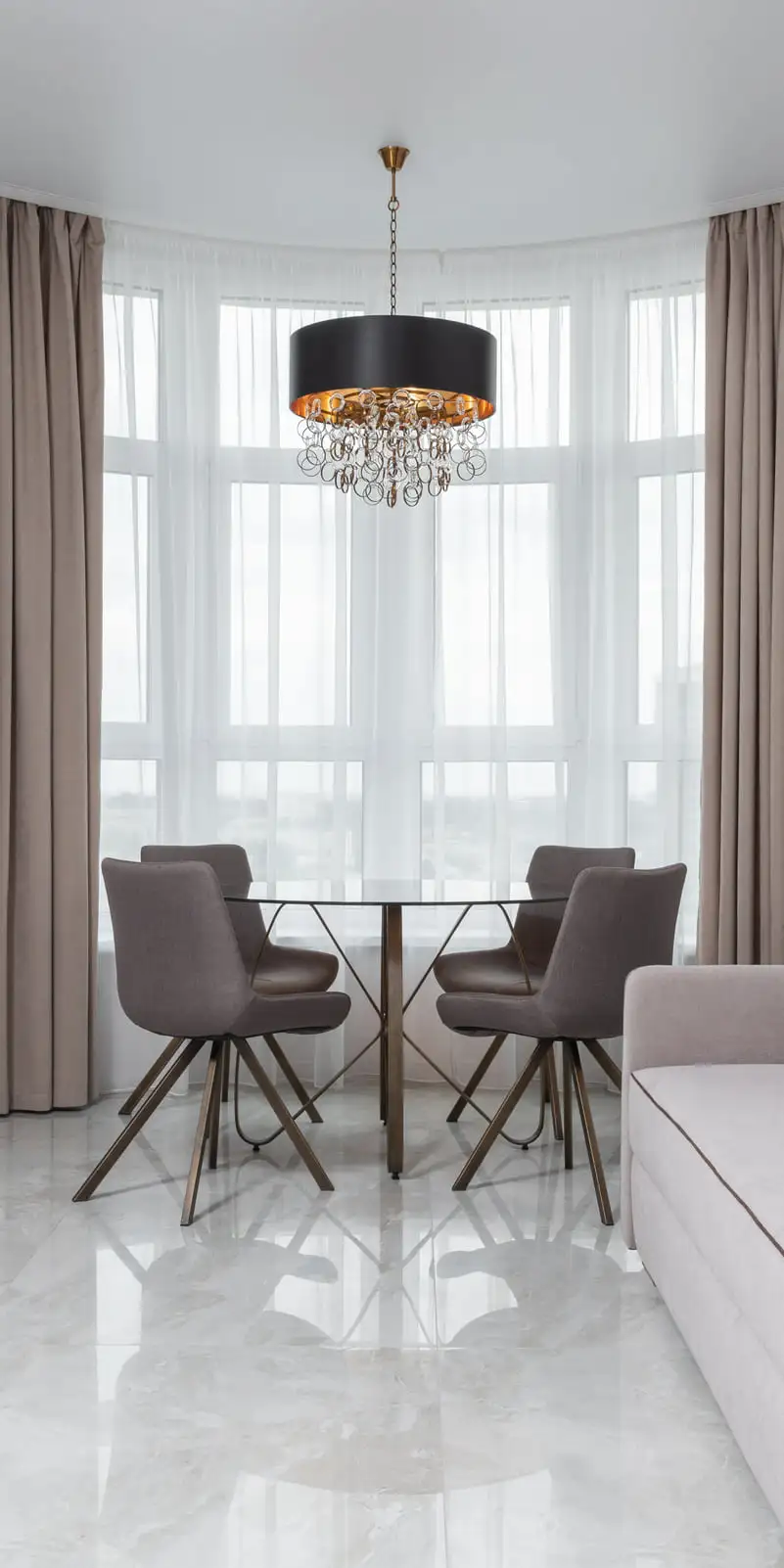 Séjour lumineux au sol de marbre blanc veiné en grand format, fenêtres en arc voilées de rideaux, table ronde et canapé clair