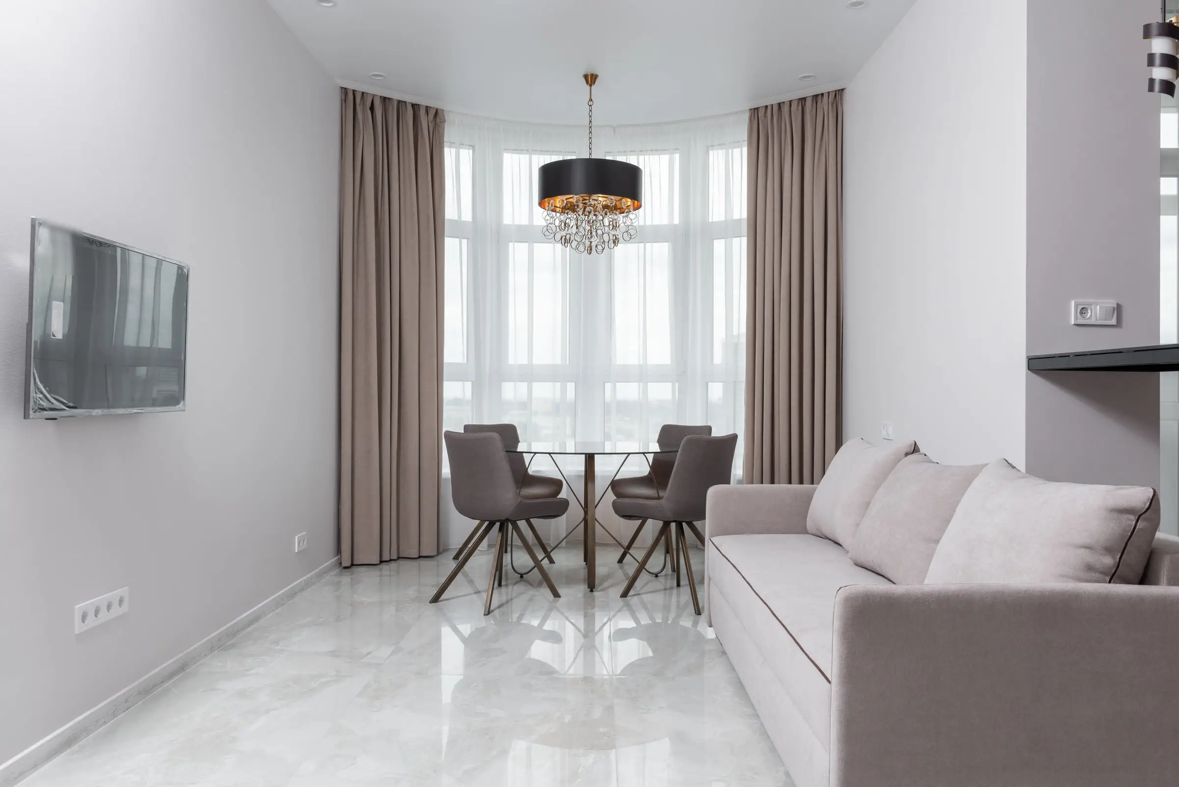 Séjour lumineux au sol de marbre blanc veiné en grand format, fenêtres en arc voilées de rideaux, table ronde et canapé clair